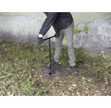 Osoba vrtá díru do země pomocí zemního vrtáku.