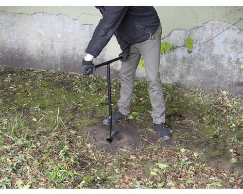 Osoba vrtá díru do země pomocí zemního vrtáku.