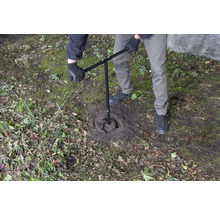 Osoba používá zemní vrták k vyvrtání díry do země.