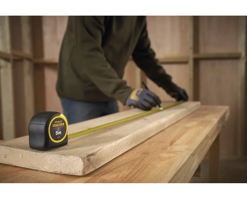 Řemeslník měří dřevěnou desku svinovacím metrem Stanley Fatmax, délka 5 metrů.