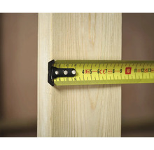 Žlutý svinovací metr Stanley měří kus dřeva.