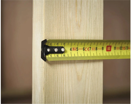 Žlutý svinovací metr Stanley měří kus dřeva.