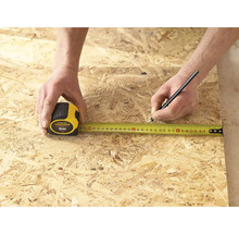 Osoba měří kus dřeva pomocí svinovacího metru Stanley Fatmax o délce 5 metrů a označuje jej tužkou.