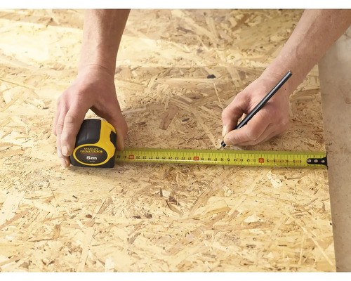 Osoba měří kus dřeva pomocí svinovacího metru Stanley Fatmax o délce 5 metrů a označuje jej tužkou.