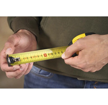 Osoba drží v ruce žlutý svinovací metr.