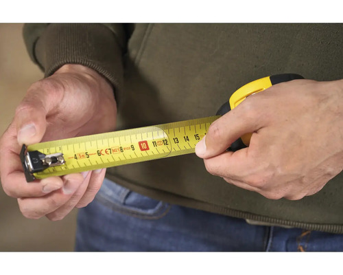 Osoba drží v ruce žlutý svinovací metr.