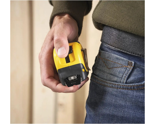 Osoba drží žlutý svinovací metr s klipem na opasek.