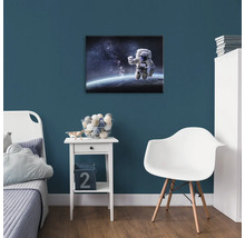 Dětský pokoj s obrázkem astronauta na zdi, noční stolek a židle.