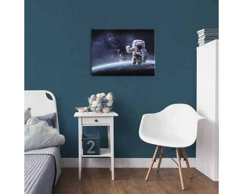 Dětský pokoj s obrázkem astronauta na zdi, noční stolek a židle.