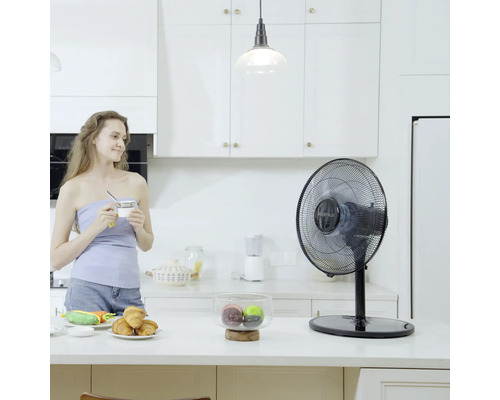 Stolní ventilátor ve světlé kuchyni se ženou držící šálek
