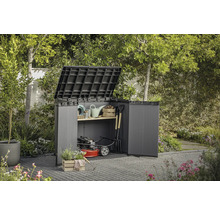 Zahradní skříň s otevřenými dveřmi a vyklopeným víkem, vyplněná zahradním nářadím a sekačkou na trávu