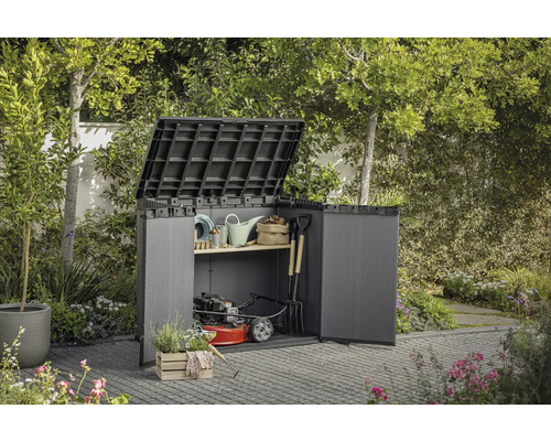 Zahradní skříň s otevřenými dveřmi a vyklopeným víkem, vyplněná zahradním nářadím a sekačkou na trávu