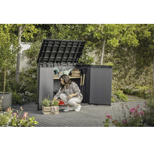 Zahrada se ženou klečící před otevřenou zahradní skříní, ve které je uloženo zahradní nářadí.