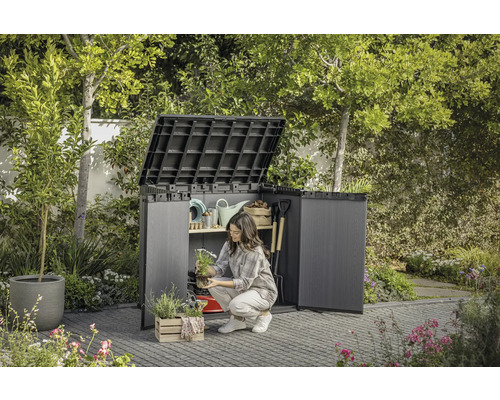 Zahradní scéna s otevřenou skříní na nářadí, do které žena ukládá zahradní náčiní.