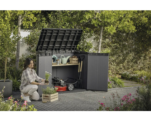 Žena sází květiny před otevřenou zahradní skříní se zahradním nářadím