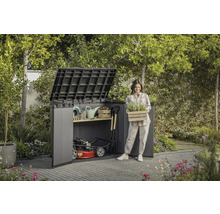 Zahradní scéna s domkem na nářadí, zahradním nářadím a ženou držící bednu s rostlinami.