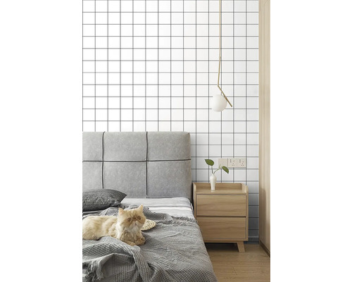 Ložnice s postelí, nočním stolkem, lampou a tapetou se čtvercovým vzorem.