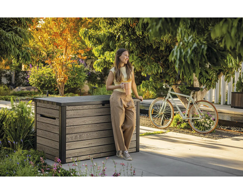 Zahradní scéna s ženou opírající se o dřevěný úložný box a držící šálek kávy.