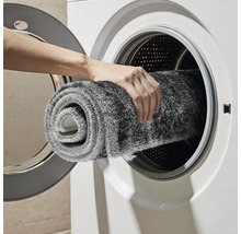 Osoba vkládá šedou koupelnovou předložku do pračky