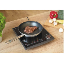 Indukční varná deska se steakem na pánvi a zeleninou na krájecí desce