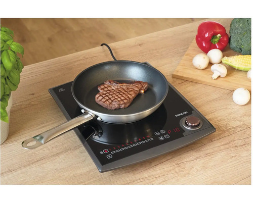 Indukční varná deska se steakem na pánvi a zeleninou na krájecí desce