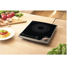 Indukční varná deska na dřevěném stole s přísadami a talířem špaget.