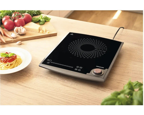 Indukční varná deska na dřevěném stole s přísadami a talířem špaget.