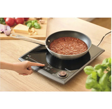 Osoba ovládá indukční vařič Sencor s pánví s rajskou omáčkou.