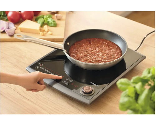 Osoba ovládá indukční vařič Sencor s pánví s rajskou omáčkou.