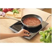 Indukční varná deska s hrncem a osobou ovládající regulátor teploty