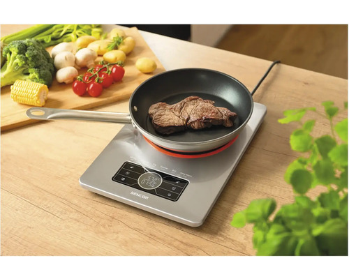Indukční varná deska s pánví a steakem na dřevěném stole