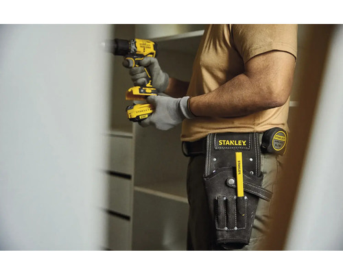 Řemeslník s akumulátorovým šroubovákem, pásem na nářadí a skládacím metrem staví skříň