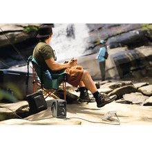 Osoba relaxuje s přenosným zdrojem energie a ventilátorem u vodopádu