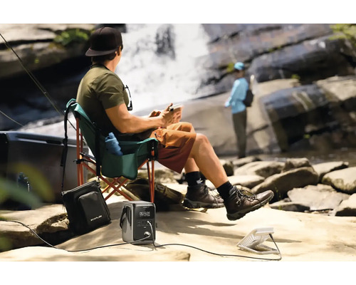 Osoba relaxuje s přenosným zdrojem energie a ventilátorem u vodopádu