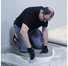 Řemeslník nanáší lepidlo na podlahu.