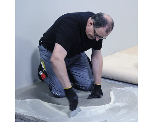 Řemeslník nanáší lepidlo na podlahu.