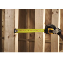 Ruka v rukavici měří dřevěný rám žlutým svinovacím metrem.