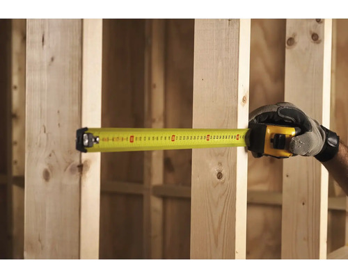 Ruka v rukavici měří dřevěný rám žlutým svinovacím metrem.