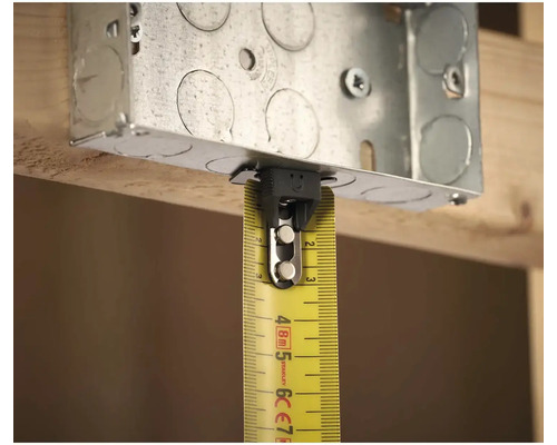 Kovová instalační krabice se žlutým svinovacím metrem pro měření na dřevěné konstrukci