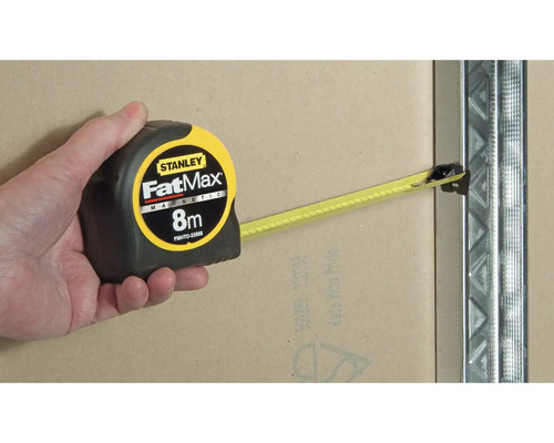 Ruka drží magnetický svinovací metr Stanley FatMax 8 metrů na kovovém sloupku.