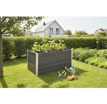 Plastový vyvýšený záhon s rostlinami, konví a zahradním nářadím na zahradě.