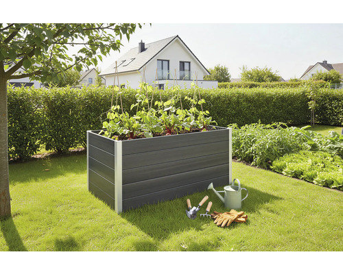 Plastový vyvýšený záhon s rostlinami, konví a zahradním nářadím na zahradě.