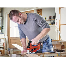 Muž řeže dřevěnou desku akumulátorovou přímočarou pilou Einhell v dílně.
