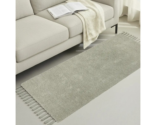 Šedý běhoun se střapci vedle pohovky s knihou