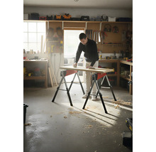 Muž brousí dřevěnou desku na dvou kozech v dílně.