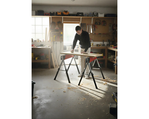 Muž brousí dřevěnou desku na dvou kozech v dílně.