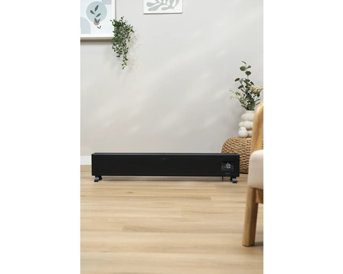 Černý konvektorový ohřívač v obývacím pokoji na dřevěné podlaze