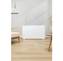 Scéna s bílým topným panelem na světlé dřevěné podlaze, vedle křesla a odkládacího stolku.