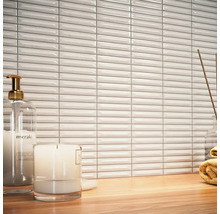 Scéna s bílými, podlouhlými obkládačkami, dávkovačem mýdla, svíčkou a ručníkem na dřevěném stole