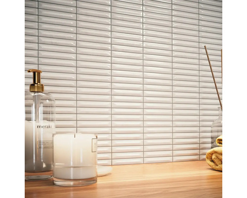 Scéna s bílými, podlouhlými obkládačkami, dávkovačem mýdla, svíčkou a ručníkem na dřevěném stole